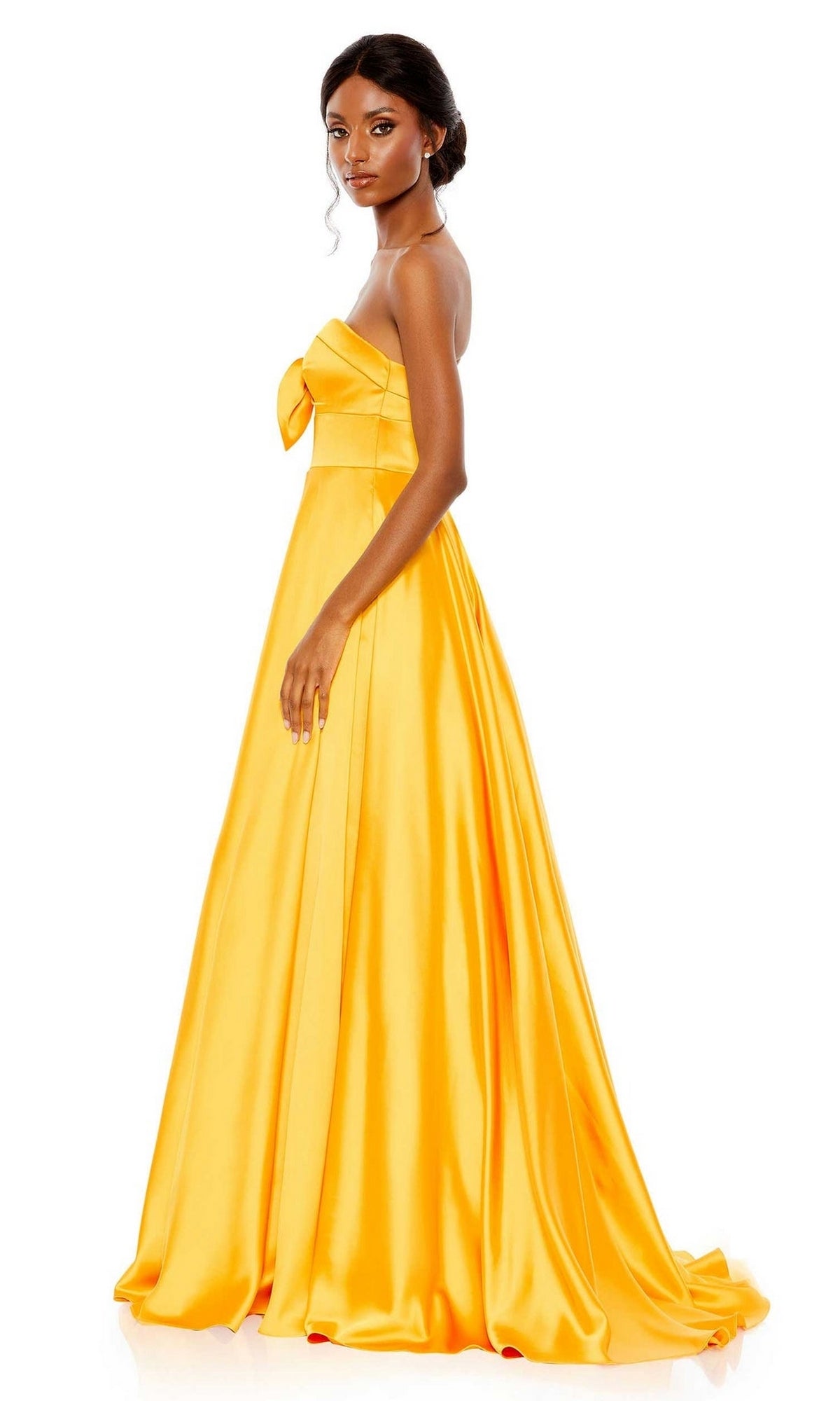 A woman models the Long Formal Dress 67995 by Mac Duggal, a marigold yellow strapless ball gown with a bow detail on the bodice, standing against a white background.